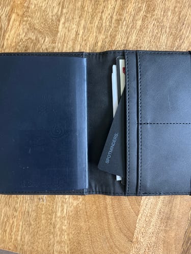 Customer's black SPOTMINDERS Tracking Card placed in an open passport holder on a wooden table.