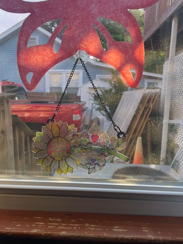 Partial view of a customer's personalized sunflower suncatcher hanging in a window, backlit by the sun.