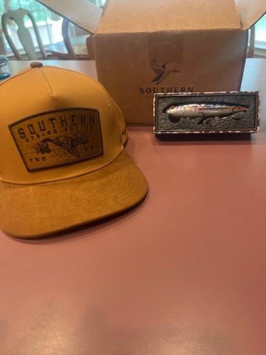 Customer's new brown Hat of the Month on a table with its box and a bonus fishing lure.