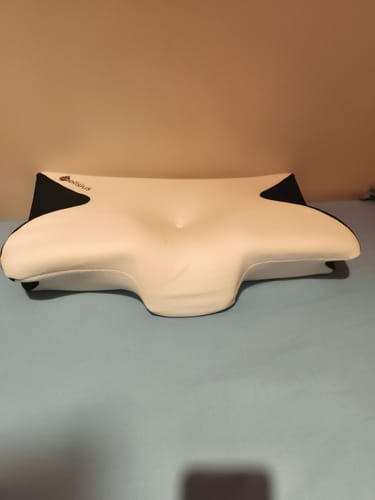 Un client montre son oreiller Papillon Cervical blanc et noir posé sur un lit.