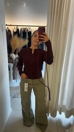 Cliente tira uma selfie no espelho, mostrando o celular com a Case bordô e alça.