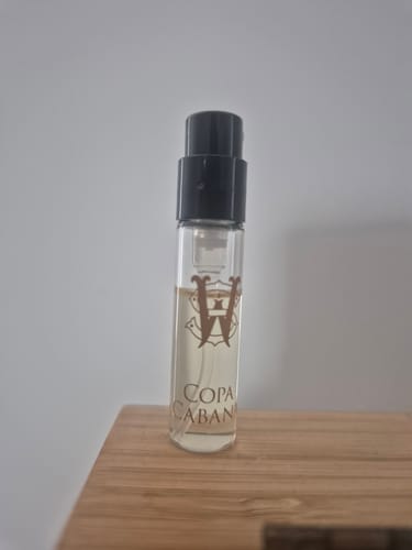 Customer's sample vial of Copacabana perfume with a black cap, standing on a wooden surface.