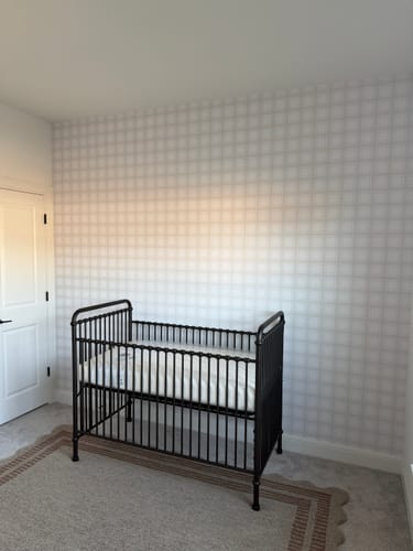 Reviewer's nursery showing the neutral Sampson Wallpaper with a grid pattern on an accent wall behind a crib.