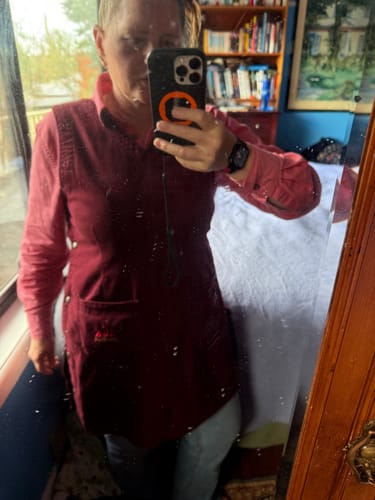 Reviewer takes a mirror selfie wearing a maroon, apron-style garment with wide straps over a pink shirt.
