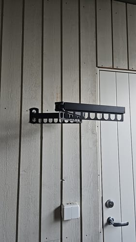 Kundes svarte, veggmonterte tørkestativ, delvis utslått på en lys vegg.