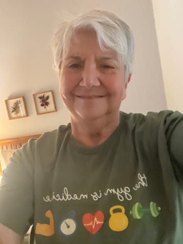 Reviewer smiling in the green Gym Medicine T-Shirt, showing the graphic print and its loose, boxy fit.