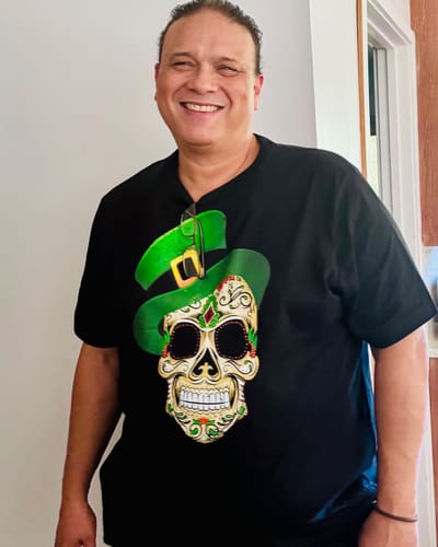 Customer smiling while wearing a black graphic t-shirt with a sugar skull in a green hat.