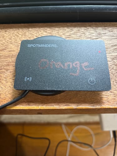 Customer's black SPOTMINDERS Tracking Card, with "Orange" written on it, sitting on a wooden surface.