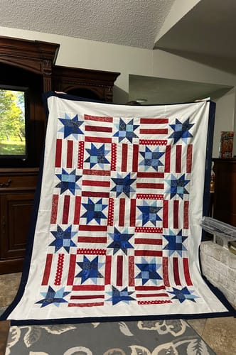 Reviewer holding up their finished Red, White, and Cute quilt, showing its patriotic star and stripe pattern.