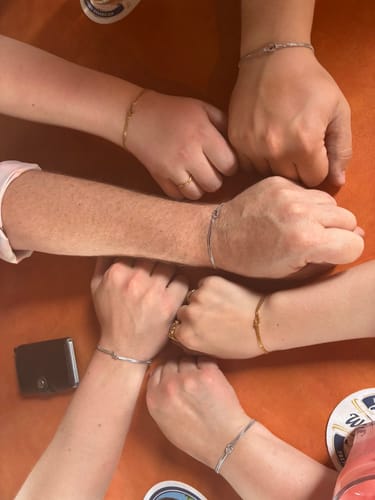 Customers' wrists together, showing matching Forever Knot Bracelets in silver and gold tones.