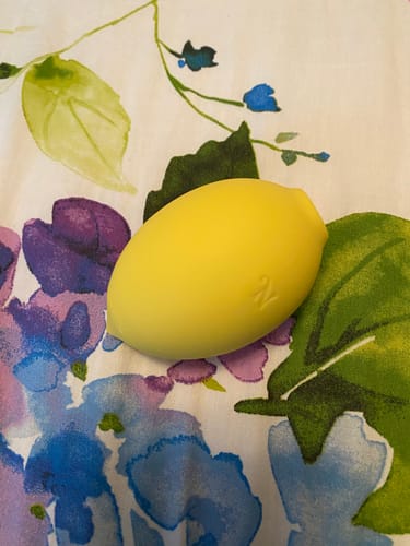 Reviewer's yellow Lem Clitoral Massager resting on a colorful floral surface.
