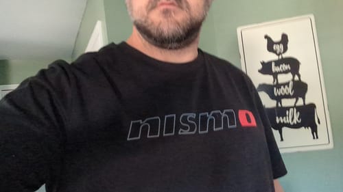 A reviewer wearing the black NISMO TEE, showing the fit and logo detail on the chest.