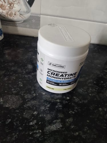 A customer's white tub of Wellcore Micronised Creatine Monohydrate, Lemon Lime flavor, on a black countertop.