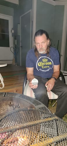 Reviewer sitting by a fire pit outdoors holding a can of Chilled Mint Nicotine Pouches.