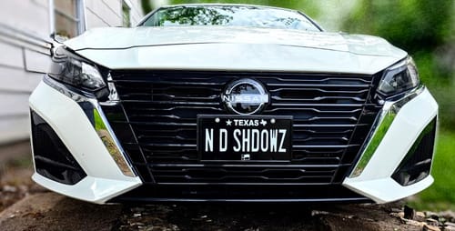 Customer's black Texas license plate customized with 'N D SHDOWZ' installed on the front of a white car.