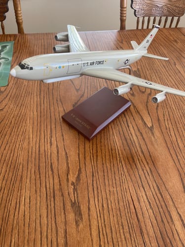 Customer's EXEC SER E-8C USAF JOINTSTAR model airplane displayed on a wooden table, with its base nearby.