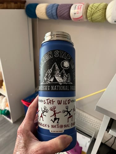 Customer holding a blue water bottle with the 'Stay Wild Petroglyphs Sticker' applied below another national park sticker.