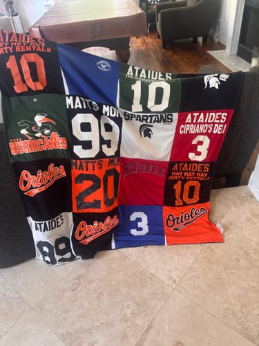 Customer's colorful Project Repat T-Shirt Quilt, made from various sports jerseys, draped over a sofa.