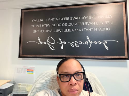 Reviewer at their home office desk with the large, framed Goodness of God Faith Sign hanging on the wall behind them.
