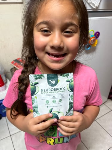 Reviewer's smiling child holds up a pouch of NeuroBrocc Gummies for Kids.