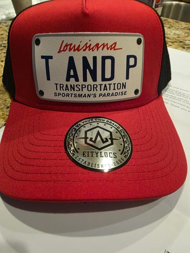 Customer's red and black Louisiana Plate Hat with a custom patch that reads 'T AND P TRANSPORTATION'.