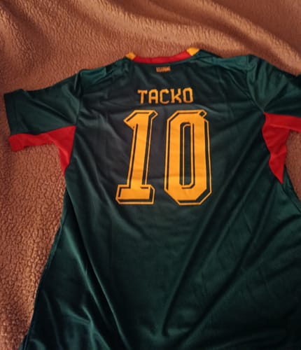 Le client montre le dos de son maillot du Sénégal, vert foncé et personnalisé avec le nom 'TACKO' et le numéro 10.