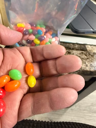 Customer holding colorful Jelly Beans in their palm, with the bag in the background.