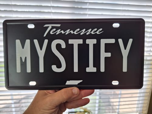 Customer holding their black Tennessee Blackout Metal License Plate customized with the text 'MYSTIFY'.