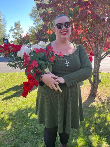 A reviewer smiling outdoors, wearing her Paw Hug Ring and holding a large bouquet.