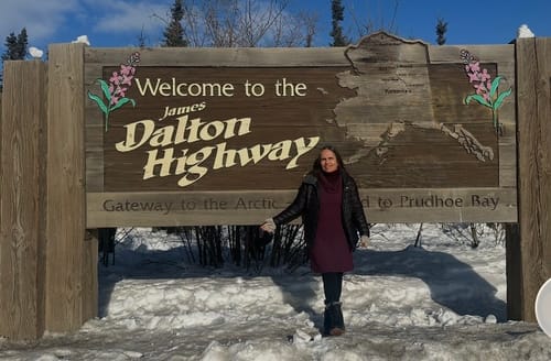 Reviewer wearing black Frost Petite Duralite® Leggings in the snow next to a highway sign in Alaska.
