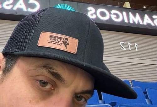 Customer's selfie showing a close-up of their black flatbill trucker hat with a custom leather patch.