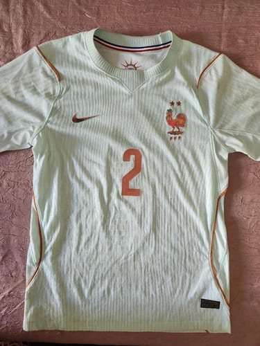 Client présentant son Maillot 2026 France Extérieur vert clair avec le numéro 2 orange, posé à plat.
