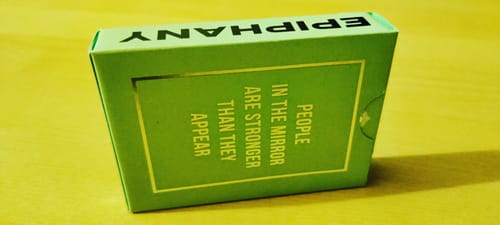 Reviewer's green Reflections Epiphany Playing Cards box with silver foil text on a wooden table.