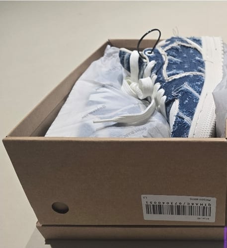 A reviewer's Street Distressed Denim Patchwork Sneaker shown partially in its original shoebox.
