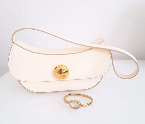Customer's Diana Petite Gold White watch lying in front of a matching off-white handbag with a gold clasp.