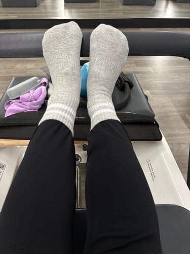 Customer wearing light grey Dual-Direction Grip Stripes socks with white stripes on a Pilates reformer.