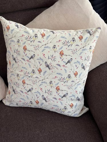 Customer's completed Linen Cushion Kit, sewn into a pillow with a bird pattern, resting on a sofa.