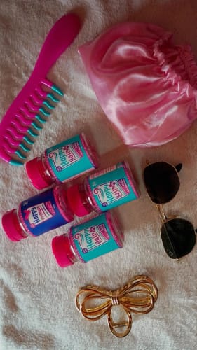 Cliente mostra seus potes de Happy Hair e Happy Collagen ao lado de um pente rosa e uma touca de cetim.