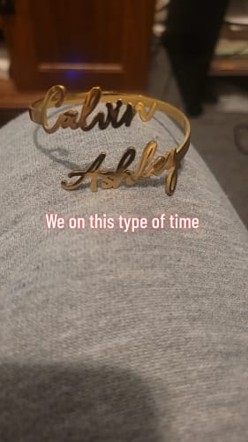 Reviewer's gold Personalized Two-Name Bangle with the names 'Calvin' and 'Ashley' resting on their lap.