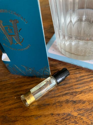 Customer's sample vial of Copacabanaproduct fragrance resting on a wooden table next to its packaging.