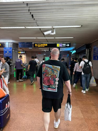 Customer wearing the black Lobster King T-Shirt, seen from behind while walking through a transit station.