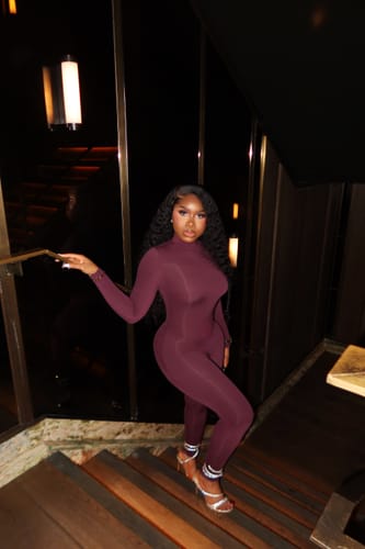 Customer posing on a staircase while wearing the maroon Naked Turtleneck Stirrup Jumpsuit.