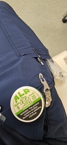 Customer's can of ALP Spearmint nicotine pouches resting on the pocket of blue cargo pants.