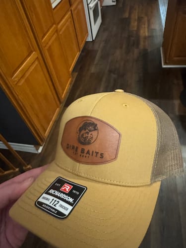Customer holding a yellow and brown Custom Leather Patch Trucker Hat with a custom fish logo on the front.