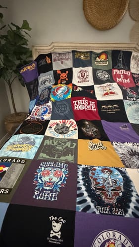 Customer's colorful Project Repat T-Shirt Quilt with many shirt designs, draped over a bed headboard.