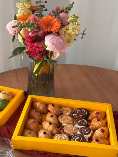 Recenzent prezintă Platoul Croissante & Cinnamon Rolls într-o cutie galbenă pe o masă.