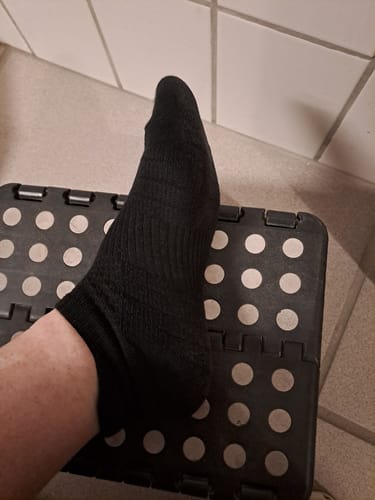 En kundes fod, der har en sort ankelstrømpe i bambus på, hviler på en skammel.