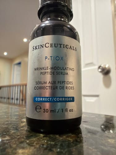 Reviewer's bottle of SkinCeuticals P-TIOX serum, a dark bottle with a silver label, resting on a dark countertop.