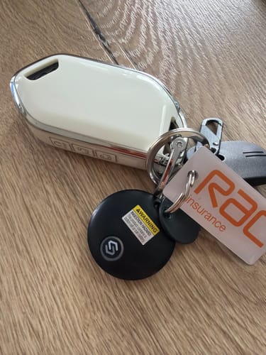 Customer's black SmartTag attached to a car key on a keychain, resting on a wooden surface.