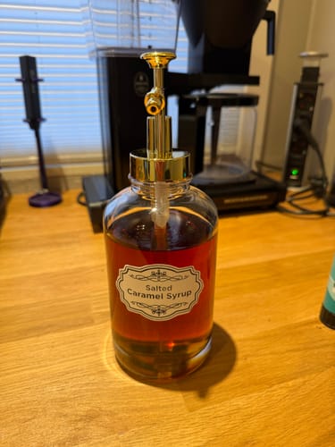Anmelderens sirupdispenser med gullpumpe står på en kjøkkenbenk i tre, med en kaffetrakter i bakgrunnen.
